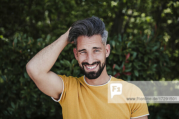 Smiling bearded man with hand in hair at park