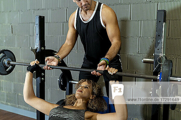 Männlicher Sportler hilft seiner Freundin beim Gewichtheben im Fitnessstudio