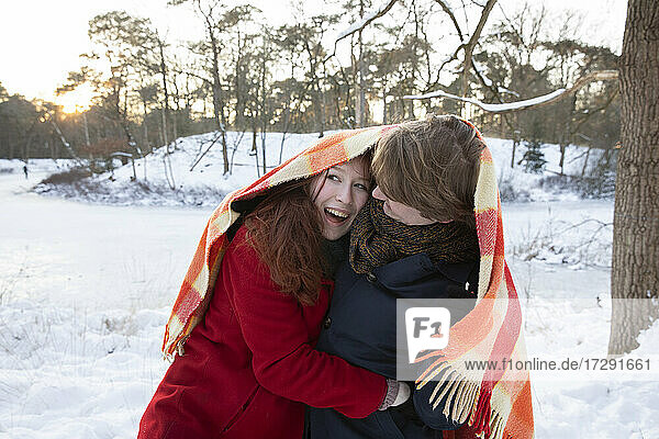 Cheerful young couple enjoying while wrapping in blanket during winter