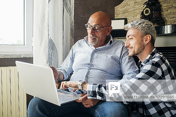 Smiling son guiding father using laptop at home