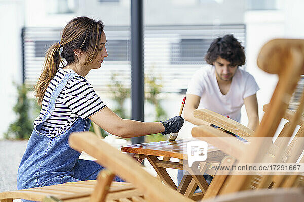 Mid erwachsene Frau poliert Holztisch während Freund im Hintergrund