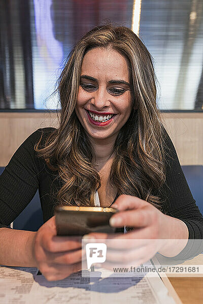 Glückliche Frau benutzt Handy im Restaurant