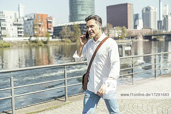 Businessman with crossbody bag talking on mobile phone during sunny day