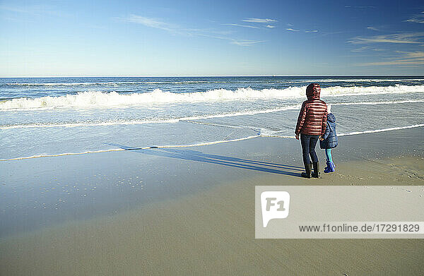 Mother with daughter looking at horizon while standing at beach