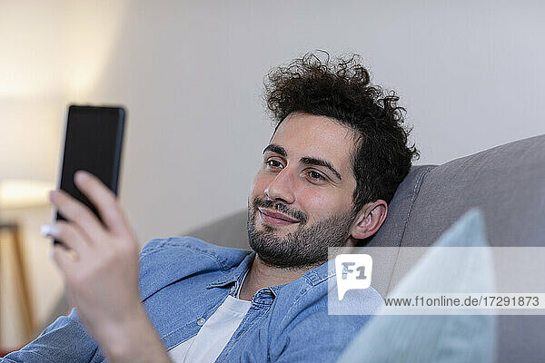 Lächelnder Mann mit Smartphone im Wohnzimmer zu Hause