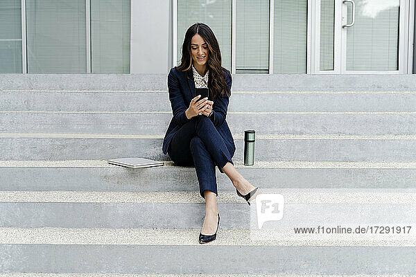 Eine Unternehmerin benutzt ein Mobiltelefon  während sie auf einer Treppe sitzt