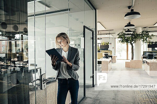 Eine Unternehmerin benutzt ein digitales Tablet und lehnt sich an eine Glaswand
