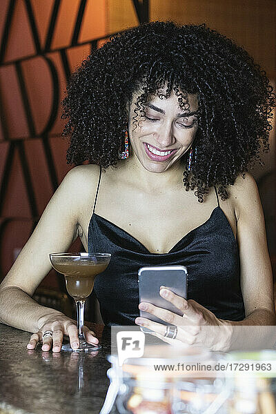 Lächelnde Frau  die ein Mobiltelefon bei einem Getränk im Restaurant benutzt
