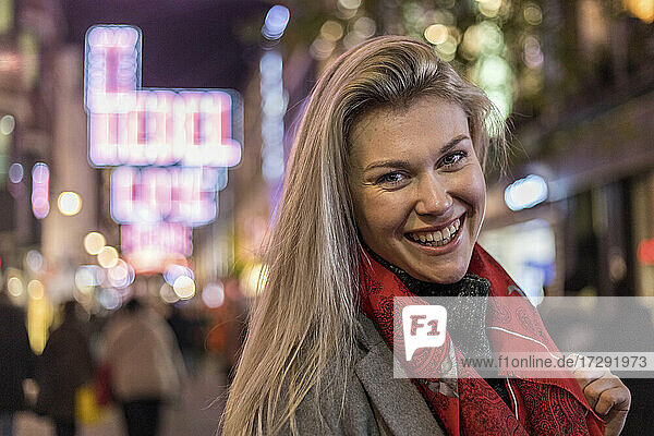 Fröhliche blonde Frau mit rotem Schal in der Stadt stehend