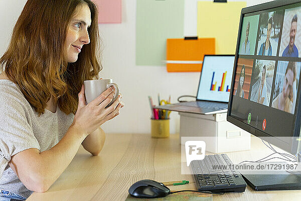Freiberuflerin hält Tasse während eines Videogesprächs am Computer im Home Office