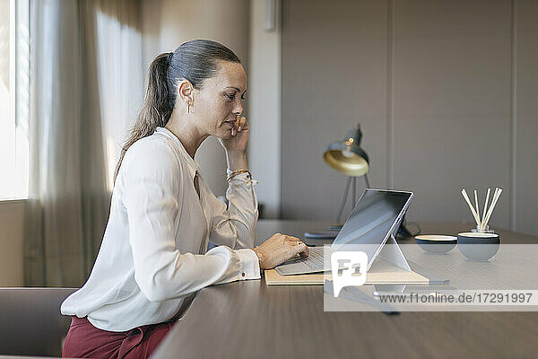 Female entrepreneur using laptop while sitting at desk in office