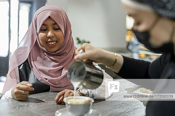 Lächelnde Frau wartet  während die Kellnerin in einem Café Milch in eine Tasse gießt