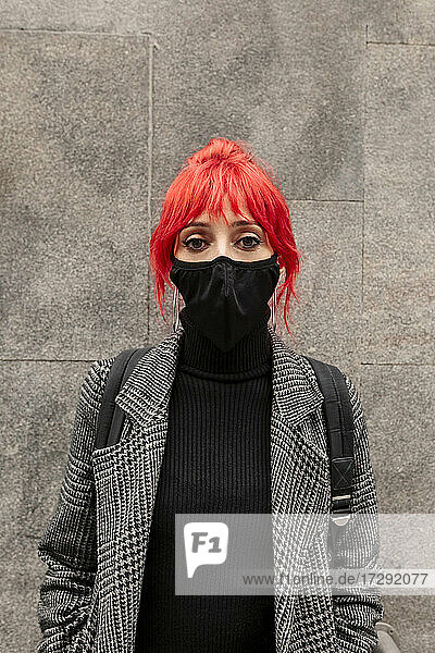 Redheaded woman wearing protective face mask standing in front of wall during COVID-19