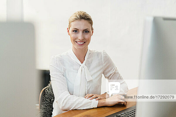 Schöne lächelnde blonde Geschäftsfrau sitzt am Schreibtisch im Büro