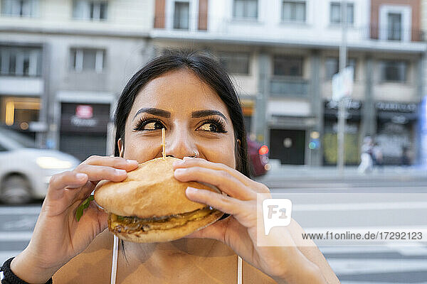 Junge Frau isst einen Hamburger in einem Straßencafé in der Abenddämmerung