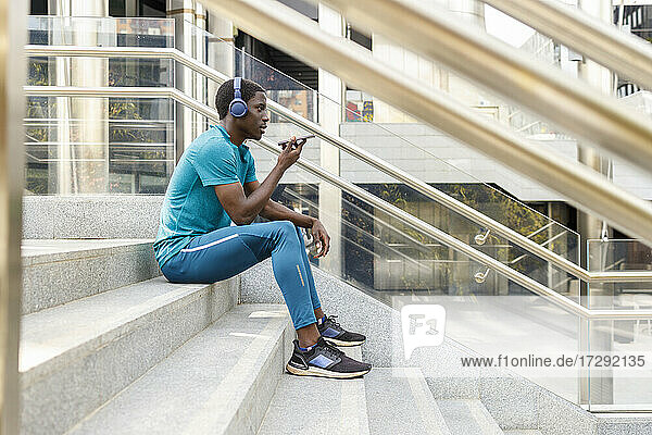 Man wearing headphones sending voicemail while sitting on staircase