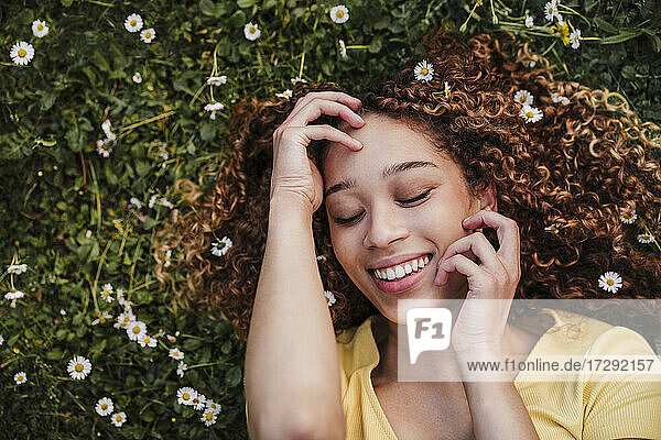 Lächelnde junge Frau mit geschlossenen Augen auf einer Wiese liegend