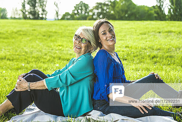 Senior woman sitting on picnic blanket with mid-adult woman at public park during sunny day