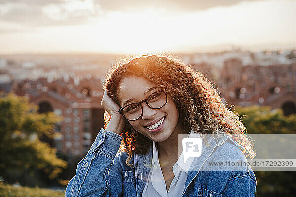 Lächelnde Frau mit Hand im Haar bei Sonnenuntergang