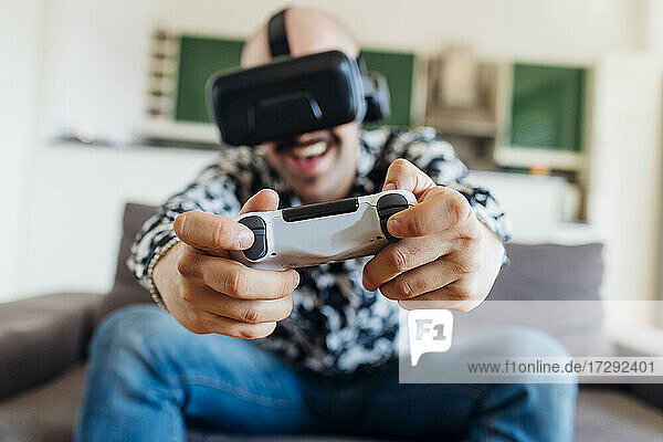 Glücklicher Mann mit virtuellem Headset spielt ein Videospiel auf dem Sofa