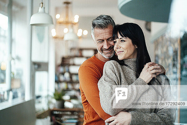 Mature man embracing woman from behind while standing in coffee shop