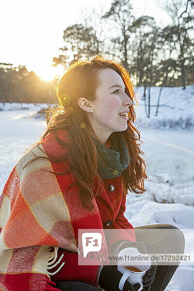 Junge Frau hält Kaffeetasse und schaut im Winter weg