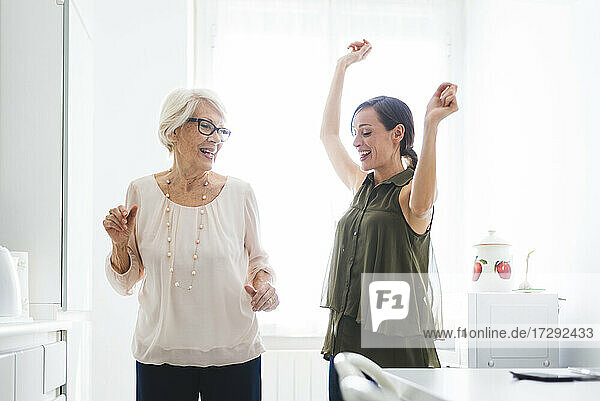 Glückliche Enkelin und Großmutter tanzen zusammen in der Küche zu Hause