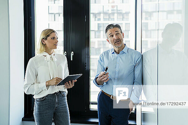 Mature businessman looking at white board while planning strategy with female professional in office