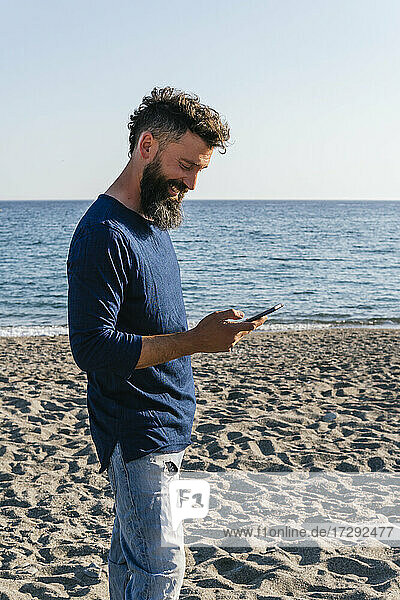 Lächelnder Mann  der am Strand stehend ein Mobiltelefon benutzt