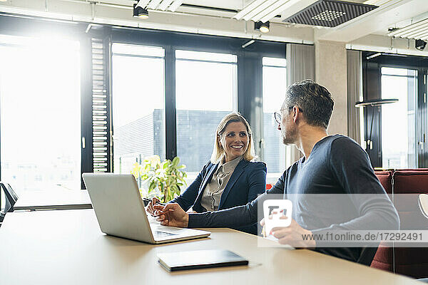 Lächelnde Geschäftsfrau mit Blick auf einen männlichen Kollegen  der in einem kreativen Büro diskutiert