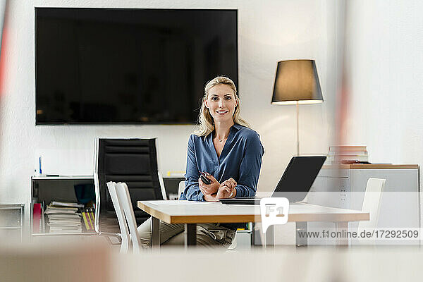 Blonde Geschäftsfrau sitzt mit Laptop am Schreibtisch im Büro
