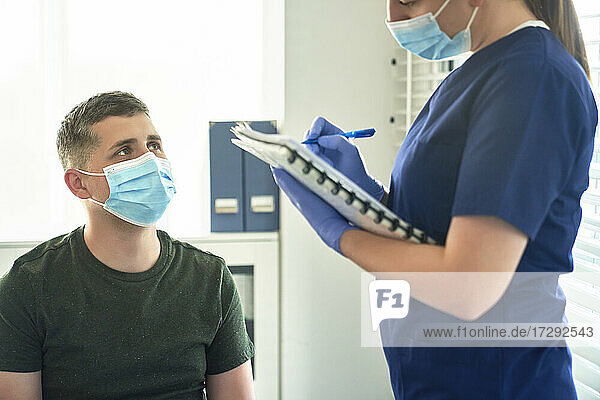 Ärztin mit Gesichtsschutzmaske bei der Befragung eines Patienten vor der Impfung in einer Klinik