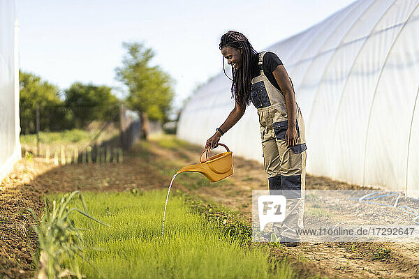 Bäuerin bewässert Pflanzen im Stehen auf einem Biohof