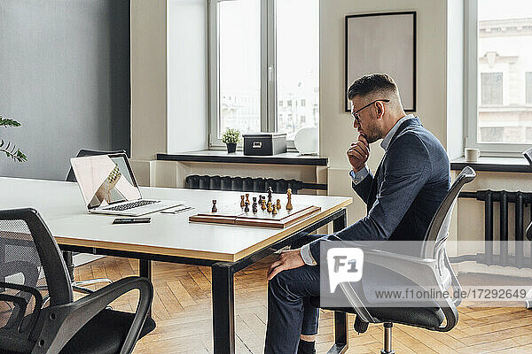 Mid adult businessman learning chess online through laptop in office