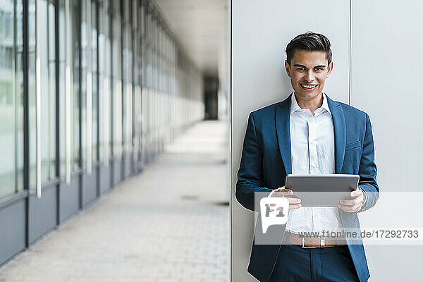 Handsome male professional with digital tablet standing at corridor