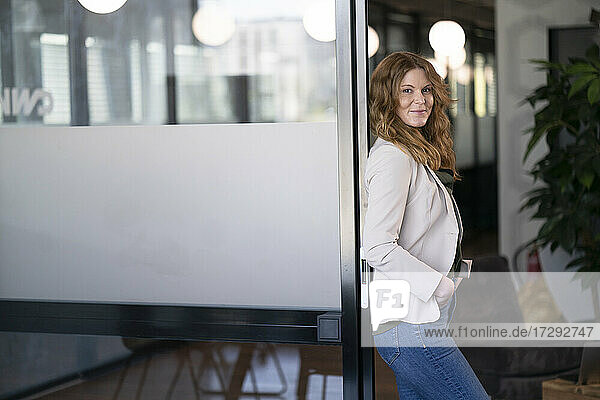 Smiling businesswoman leaning on doorway at office