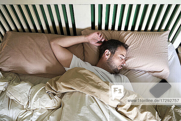 Mid adult man sleeping by mobile phone in bed