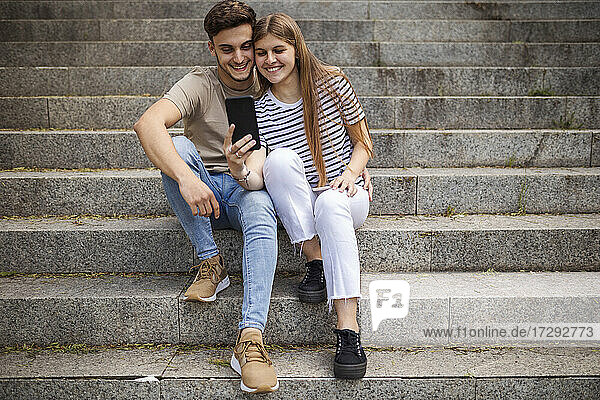 Lächelndes Paar  das ein Selfie mit dem Mobiltelefon macht  während es auf den Stufen sitzt