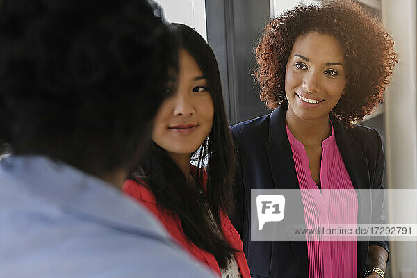 Lächelnde Geschäftsfrauen betrachten einen männlichen Kollegen  der im Büro diskutiert