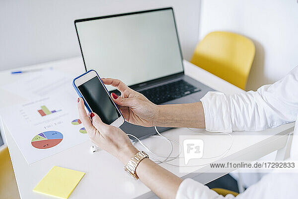 Frau benutzt Smartphone am Laptop im Büro zu Hause