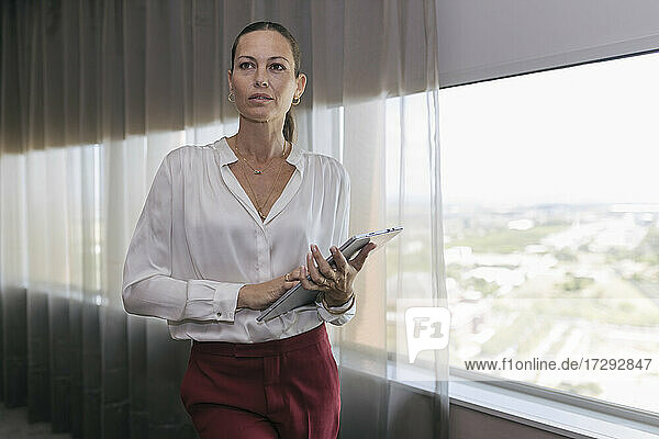 Unternehmerin stehend mit digitalem Tablet am Fenster im Büro