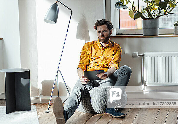 Geschäftsmann  der ein digitales Tablet benutzt  während er auf einem Hocker im Büro sitzt