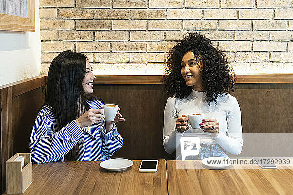 Multi-ethnic female friends talking to each other while having coffee at bar