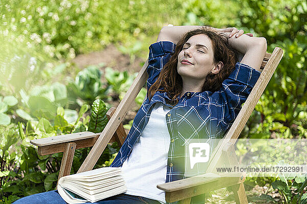 Frau mit erhobenen Armen entspannt auf einem Stuhl im Garten