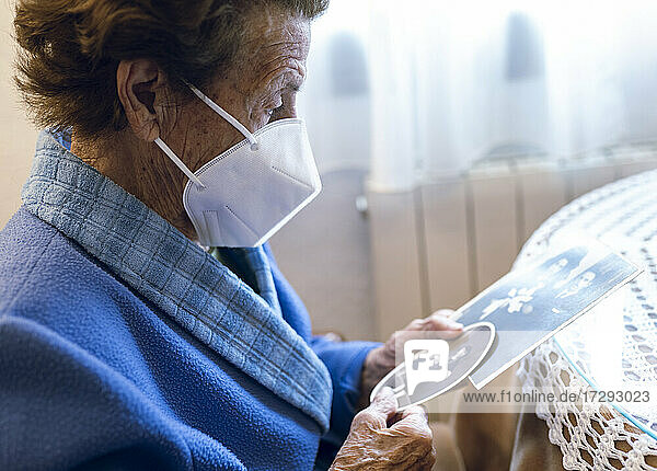 Senior woman wearing protective face mask watching old photograph at home