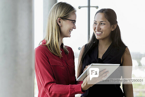 Lächelnde Geschäftsfrauen  die über eine digitale Tafel im Büro diskutieren