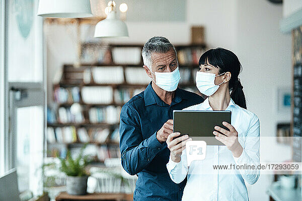 Männliche und weibliche Besitzer mit Gesichtsmaske bei der Nutzung eines digitalen Tablets in einem Café