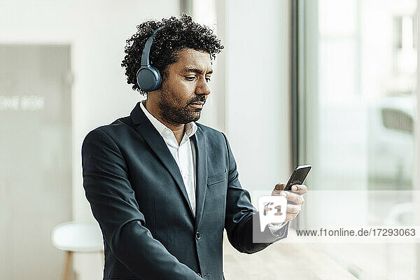 Männlicher Unternehmer  der ein Smartphone benutzt und über Kopfhörer im Büro Musik hört