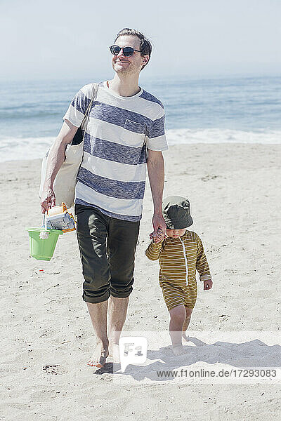 Smiling man holding son hand while walking at beach