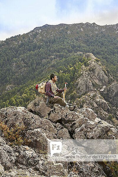 Männlicher Bergsteiger  der die Aussicht betrachtet  während er auf einem Berg sitzt